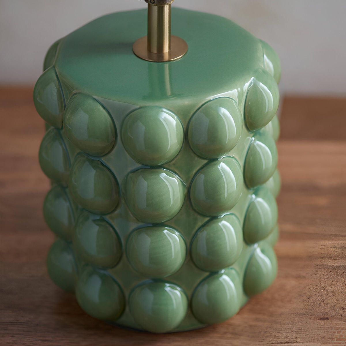 Close-up of the Endon Amberley ceramic table lamp base in glossy olive green with sculpted bobble texture and an aged brass stem, on a wooden surface.