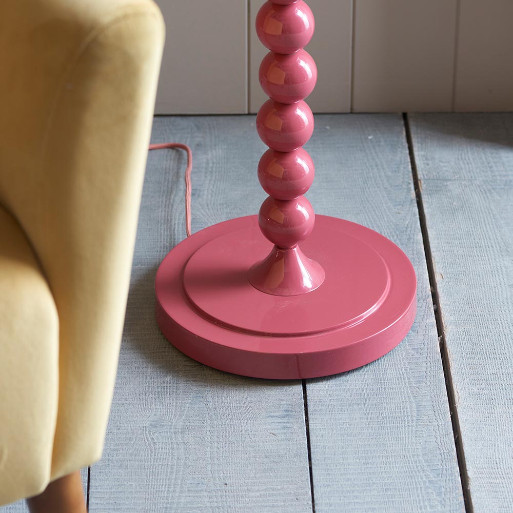 Endon Brenleigh floor lamp base in glossy pink with stacked metal spheres and a round base, shown on pale wood flooring beside a cream armchair.