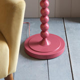 Endon Brenleigh floor lamp base in glossy pink with stacked metal spheres and a round base, shown on pale wood flooring beside a cream armchair.