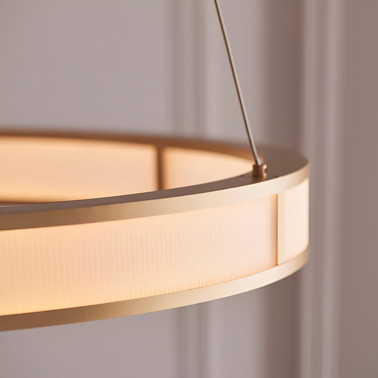 Close-up of Endon Bevley Ring Pendant in brushed gold, showing the ribbed frosted acrylic diffuser and clear suspension cable against a neutral wall.