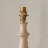Endon Brenhurst table lamp base close-up showing hand-turned natural wood profile and switched brass B22 lamp holder against a pale wall.