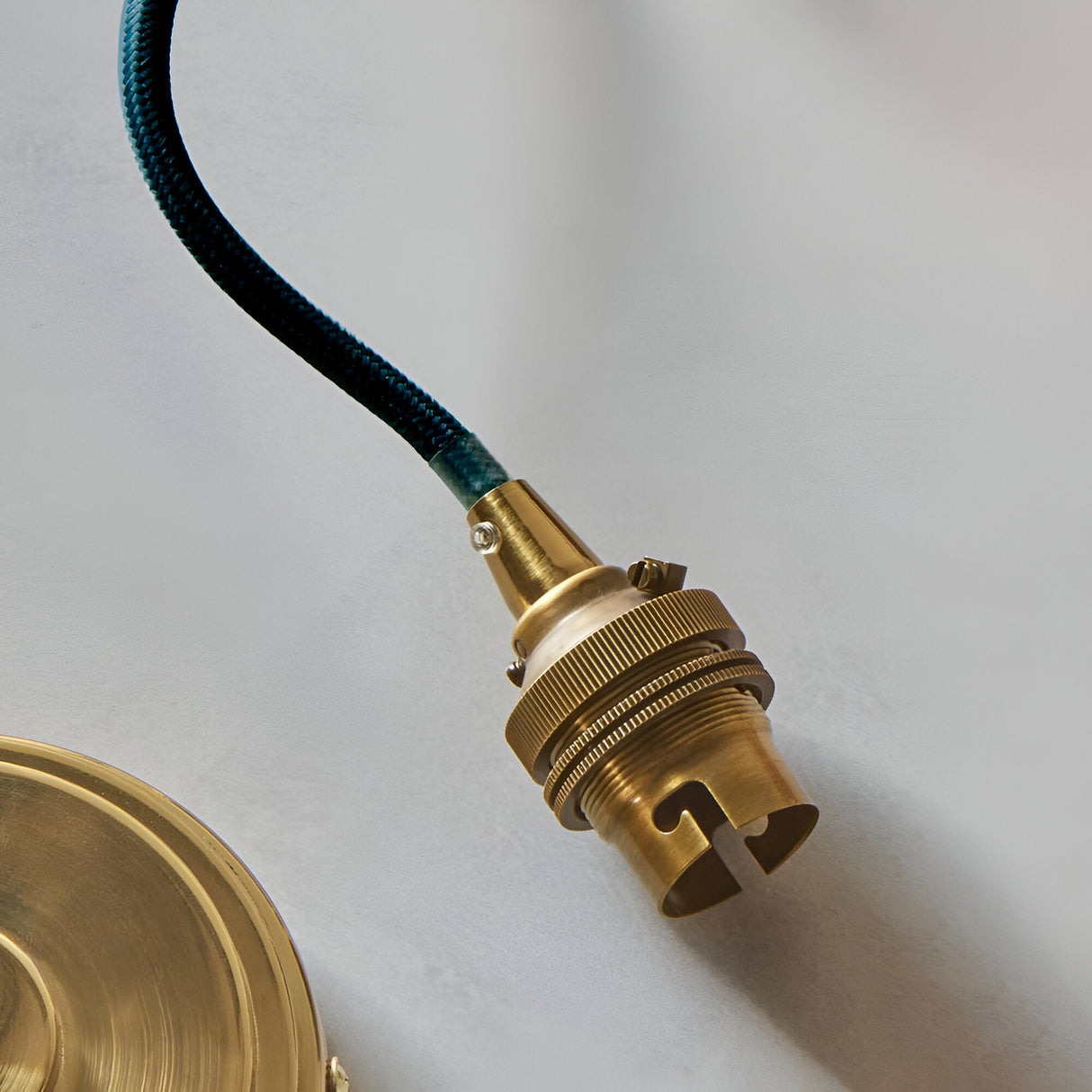 Close-up of the Endon Brackmont flex set showing the brushed aged brass B22 lampholder and blue braided fabric cable against a light background.