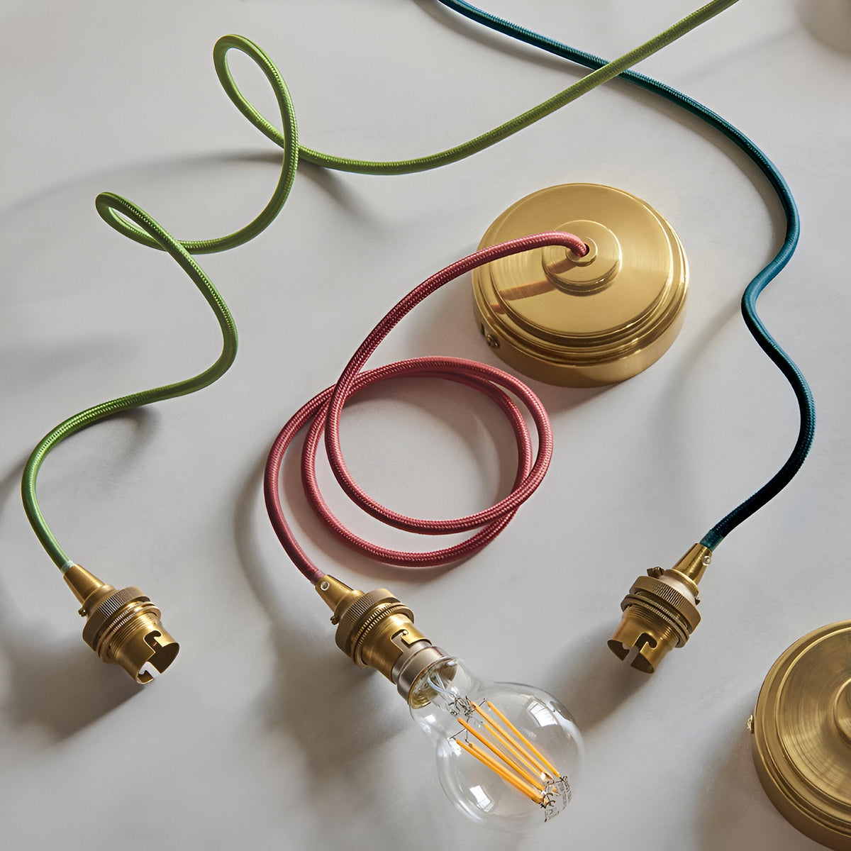Endon Brackmont flex sets with brushed brass B22 fittings and braided fabric cables in green, red and blue, shown with ceiling roses and a filament bulb.