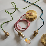 Endon Brackmont flex sets with brushed brass B22 fittings and braided fabric cables in green, red and blue, shown with ceiling roses and a filament bulb.