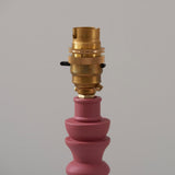 Close-up of the Endon Aldworth table lamp showing the brass B22 switched lampholder above a turned pink wood spindle base, on a light grey background.
