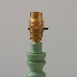 Aldworth Table Lamp base close-up in green with turned solid wood spindle base and brass B22 switched lampholder, on a plain grey background.