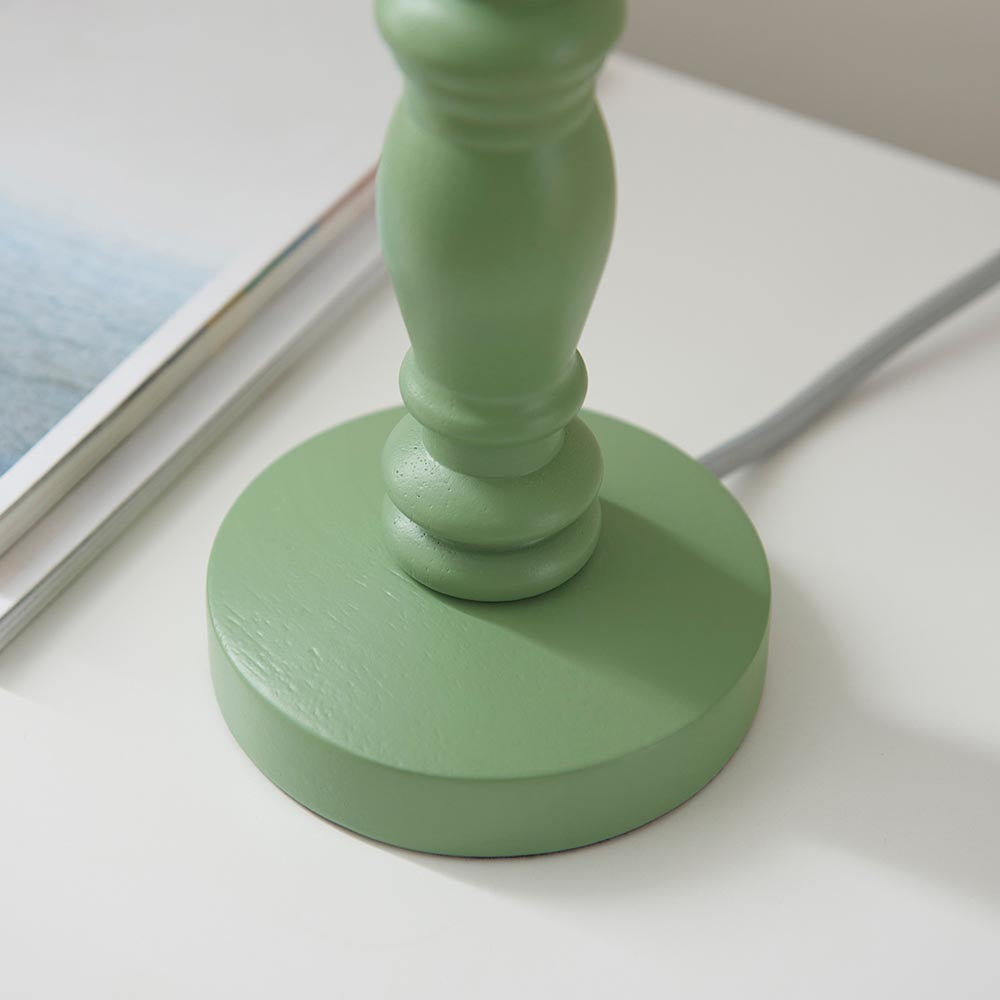 Aldworth Table Lamp base close-up, turned wood spindle in green satin finish, round base on white desk with grey flex and magazine nearby.