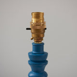Endon Aldworth table lamp close-up showing the brass B22 switched lampholder above a turned marlin blue wood spindle, on a light background.