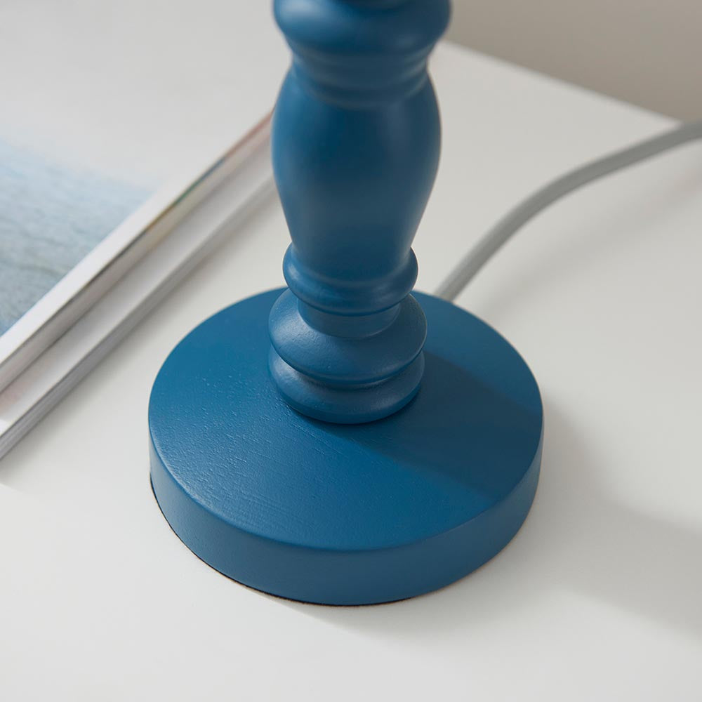 Close-up of the Endon Aldworth table lamp base in marlin blue turned wood with grey braided flex, beside a magazine on a white surface.