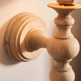 Close-up of Endon Aldworth wall light in turned natural ash with ringed backplate, spindle arm, and brass B22 lampholder mounted on a pale wall.
