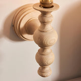 Close-up of Endon Aldworth wall light in natural ash with turned spindle detail, brass B22 lampholder, and round wall mount on a pale wall.
