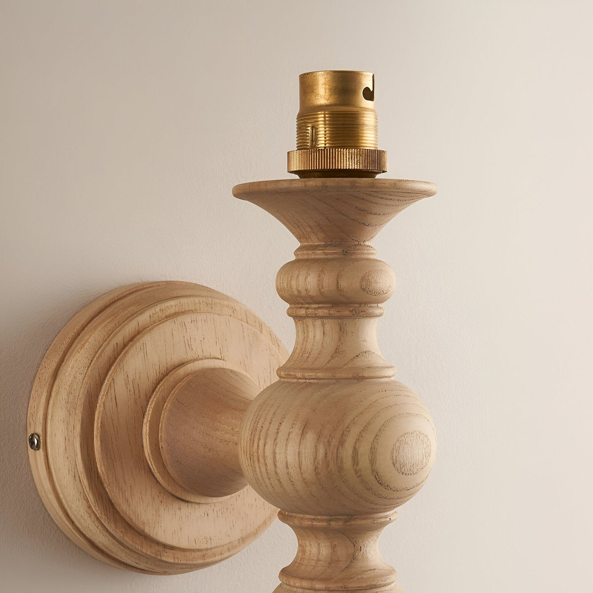 Close-up of Endon Aldworth wall light in natural ash, showing turned spindle arm, round wall plate, and brass B22 lampholder against a pale wall.