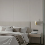 Bisel Cylinder Ribbed Glass Wall Light in gold mounted above a bedside table, with ribbed glass cylinder and curved metal sleeve, shown in a neutral-toned bedroom setting.