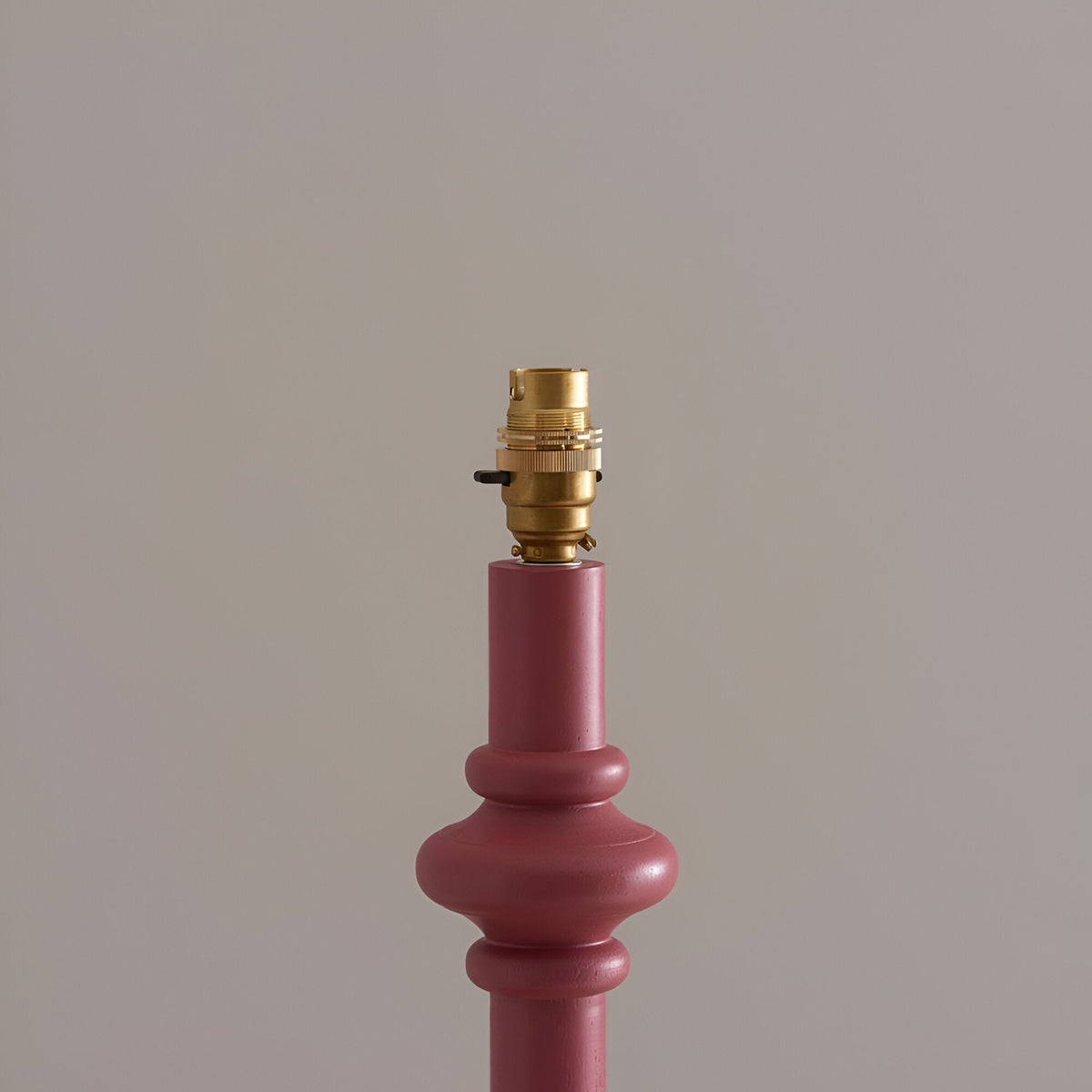 Close-up of the Endon Bevbury floor lamp's pink clay turned wood spindle top with switched brass B22 lamp holder against a neutral background.