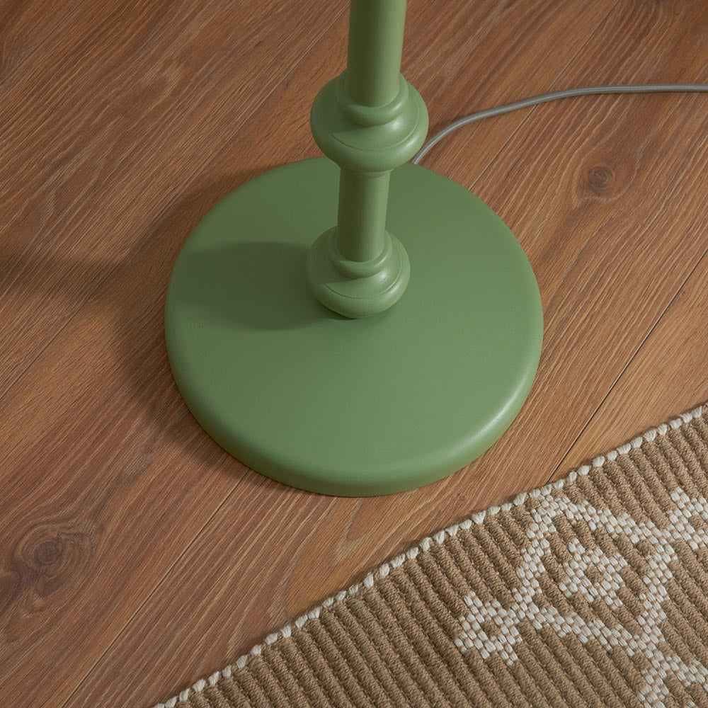 Close-up of the Endon Bevbury floor lamp base in Cotswold green with turned spindle detail and grey braided flex, on wood flooring beside a woven rug.