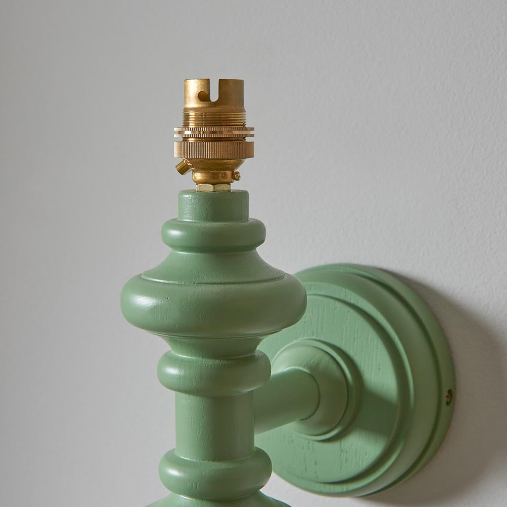 Endon Bevbury wall light close-up showing the Cotswold green turned wooden spindle, circular wall plate and exposed brass B22 lamp holder.