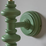 Close-up of the Endon Bevbury turned wooden spindle wall light in satin Cotswold green with a circular backplate, mounted on a pale wall.
