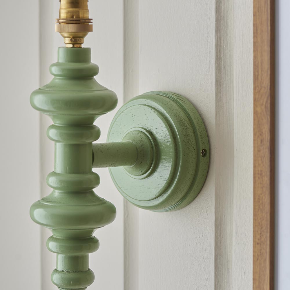 Endon Bevbury wall light close-up showing the Cotswold green turned wooden spindle and brass B22 lamp holder mounted on a panelled wall.