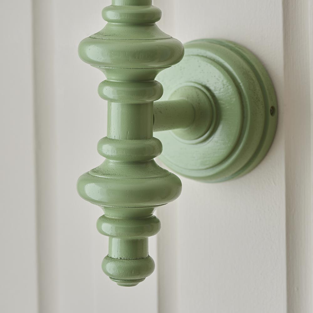 Endon Bevbury wall light close-up showing the Cotswold green turned wooden spindle and round backplate mounted on a white panelled wall.