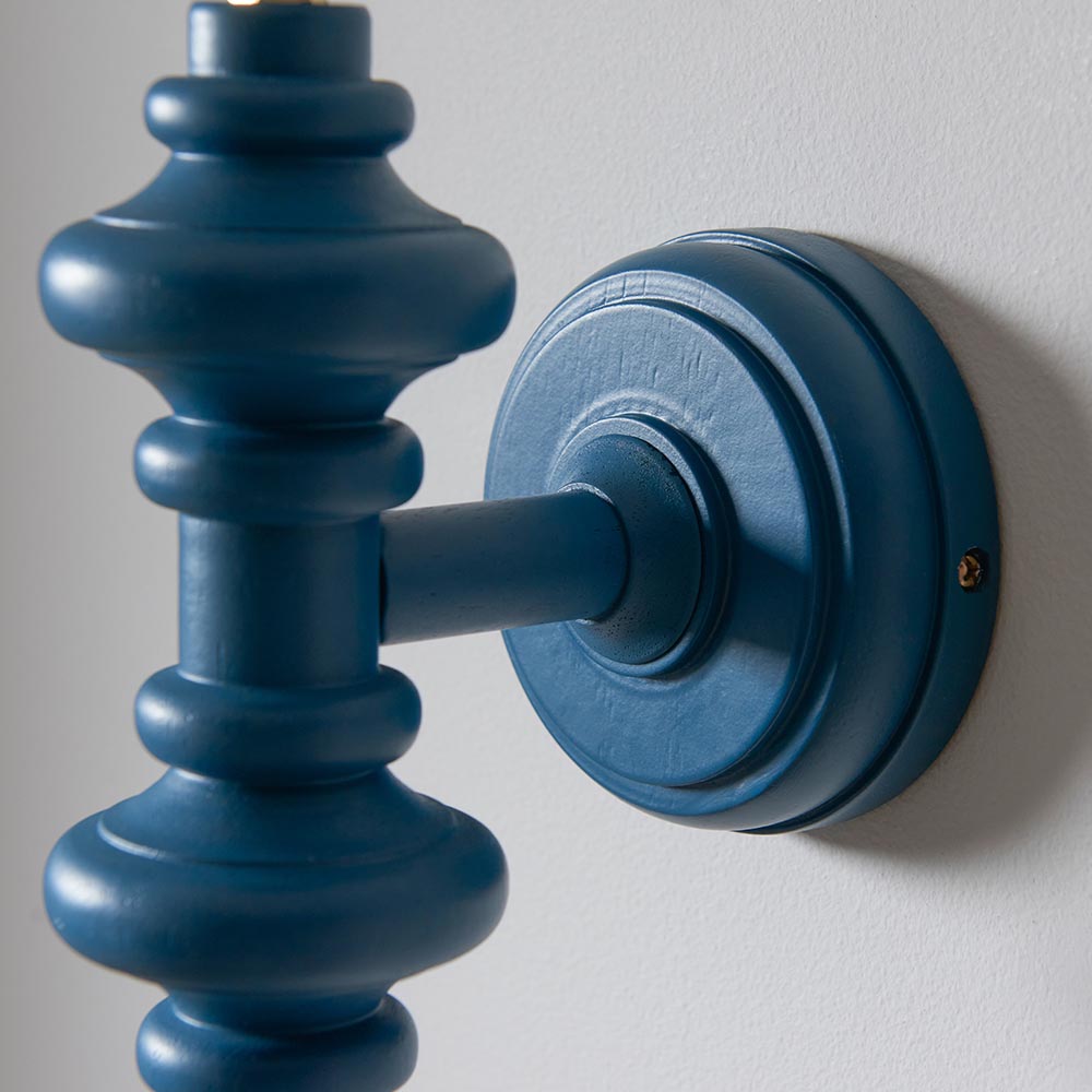 Close-up of the Endon Bevbury turned wooden spindle wall light in satin marlin blue, showing the round wall plate and mounting screw against a pale wall.