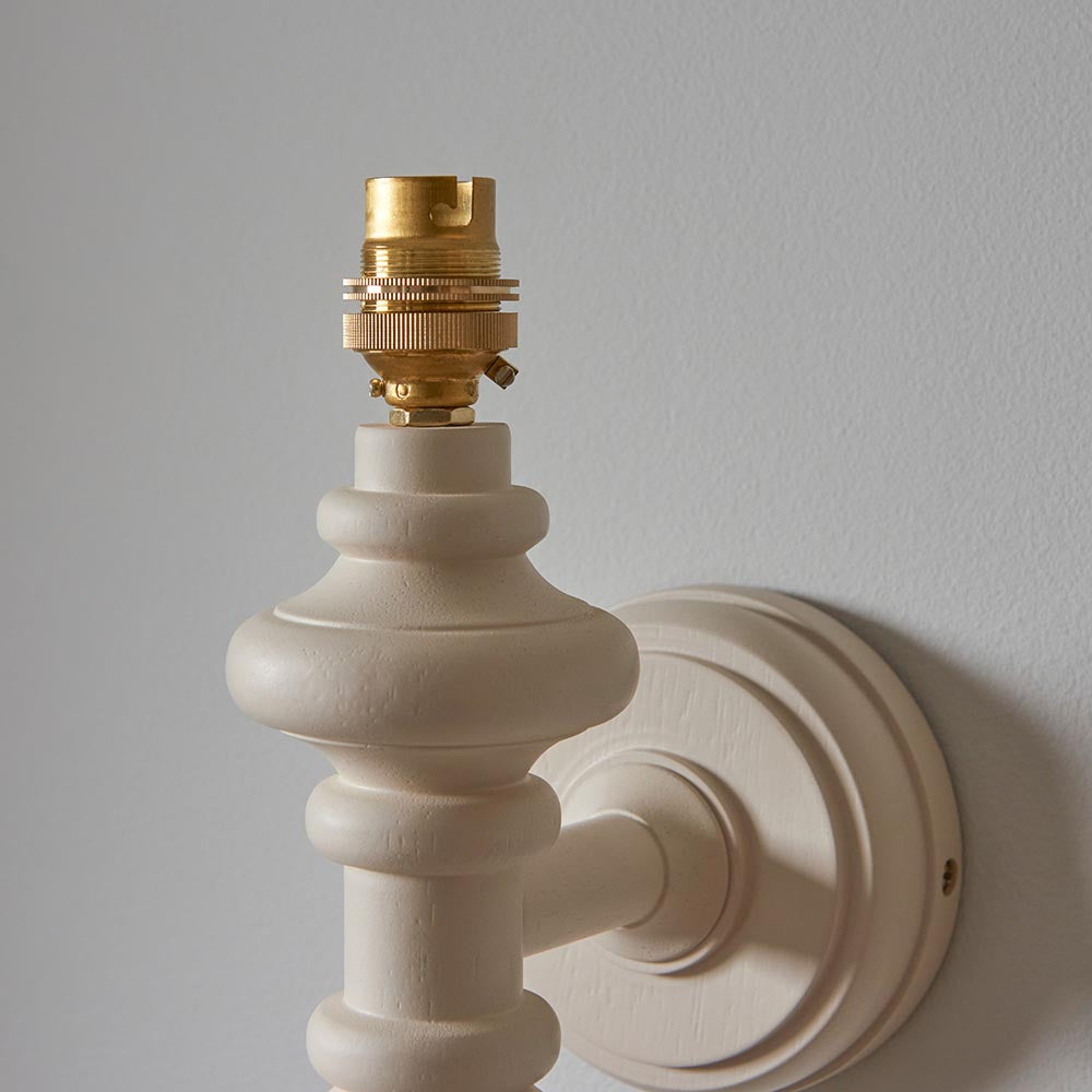 Endon Bevbury wall light with turned wooden spindle in satin almond white and exposed brass B22 lamp holder, mounted on a neutral wall.