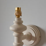 Endon Bevbury wall light with turned wooden spindle in satin almond white and exposed brass B22 lamp holder, mounted on a neutral wall.