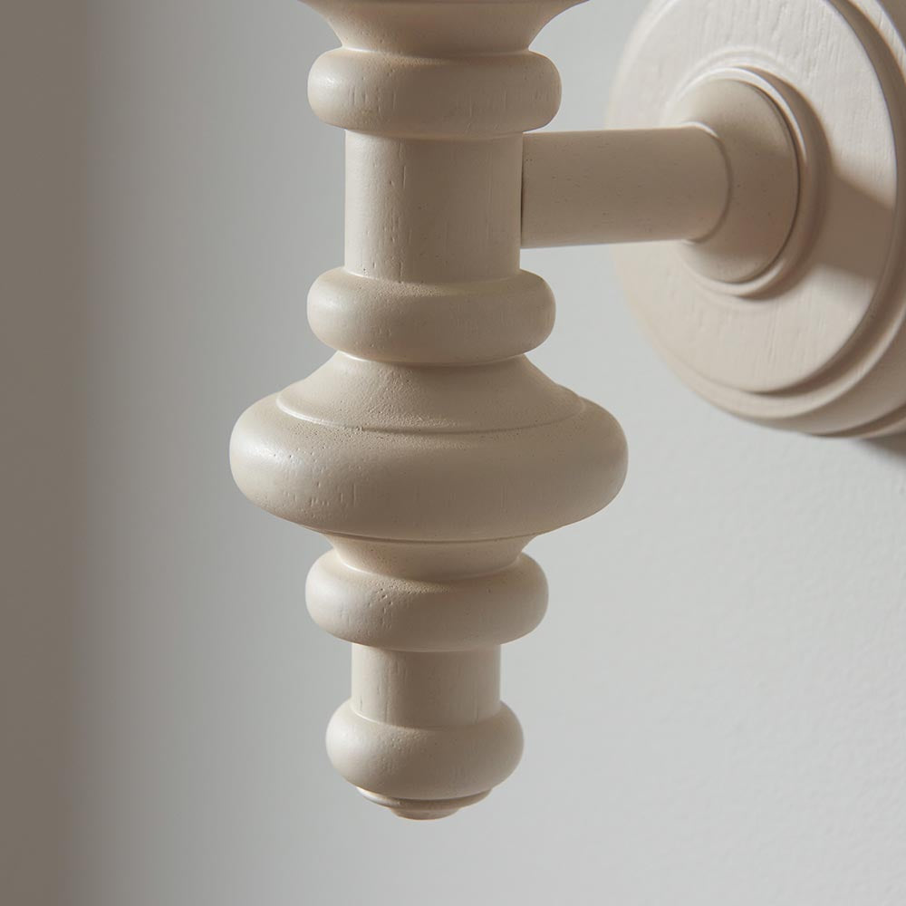 Close-up of the Endon Bevbury turned wooden spindle wall light in almond white satin finish, mounted on a round backplate against a pale wall.