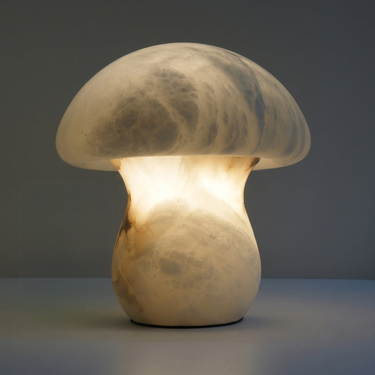 Morfia Small Mushroom Alabaster Table Lamp in Soft White, carved natural stone with dome-and-stem silhouette, glowing amber veining, shown lit against a plain grey background.