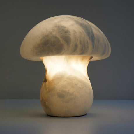 Morfia Mushroom Alabaster Table Lamp in soft white, carved from solid alabaster with a domed cap and stem glowing warmly from within, shown against a plain grey background.