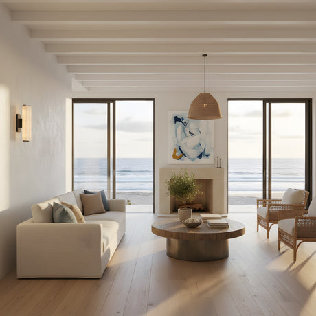 Modern living room with large windows overlooking the ocean, neutral furnishings like a white sofa and wooden coffee table, and Selvara LED Small Alabaster Double Wall Light in matte black & soft white providing gentle illumination as natural light fills the space.