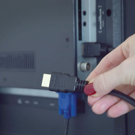 Hand holding AVSL AV:Link 4K HDMI lead with gold plated plug, being connected to the rear HDMI port of a TV above a blue VGA socket.