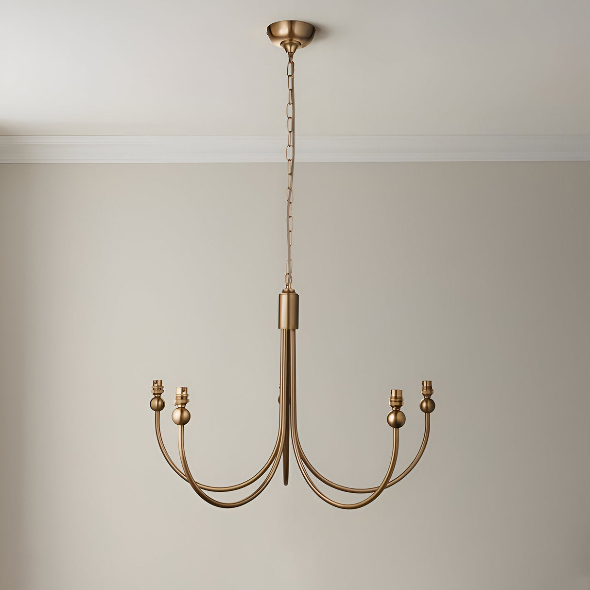 Endon Cliffleigh 5 light chandelier in brushed aged brass with curved J-shaped arms and B22 holders, hung from a chain against a neutral wall.