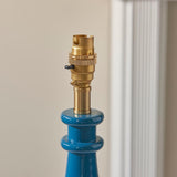 Close-up of Endon Carlworth table lamp base in gloss blue resin with brass B22 switched holder, turned spindle shape, beside a white fluted column.