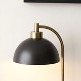 Endon Ashmont table lamp close-up showing matt black dome shade and curved antique brass stem against a pale wall.