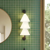 Boga LED Cone Glass Linear Wall Light in matt black, with three stacked white glass cone shades glowing warm white on a green tiled wall beside a round mirror.