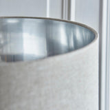 Close-up of the Endon Brenley floor lamp shade showing a natural linen exterior and brushed chrome metallic inner lining against a pale panelled wall.