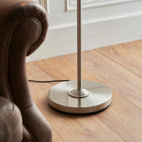 Endon Brenley floor lamp base in brushed chrome with circular tiered plinth and black cable, set on wood flooring beside a brown leather armchair.