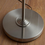 Close-up of the circular tiered base and slim stem of the Endon Brenley floor lamp in brushed chrome, shown on wood flooring.