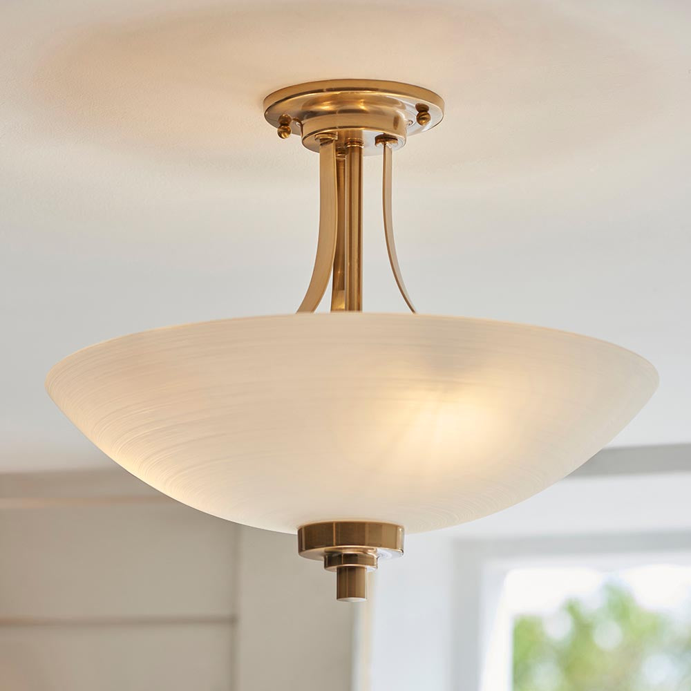 Carlton 3 Light Flush Ceiling Light in brushed aged brass, with a frosted glass bowl shade and three lamp fittings, shown illuminated near a room ceiling.