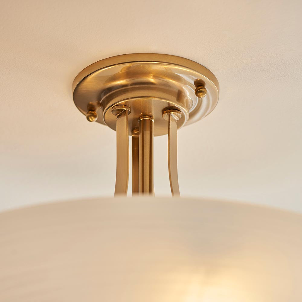 Close-up of the Carlton 3 Light Flush Ceiling Light in brushed aged brass with round ceiling plate, brass rods and opal glass shade.