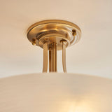 Close-up of the Carlton 3 Light Flush Ceiling Light in brushed aged brass with round ceiling plate, brass rods and opal glass shade.