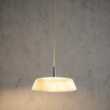 Bonn Alabaster Drum Pendant Light with a shallow, tapered veined alabaster shade on a slim metallic stem and cream textile cable, lit warm white against a grey background.