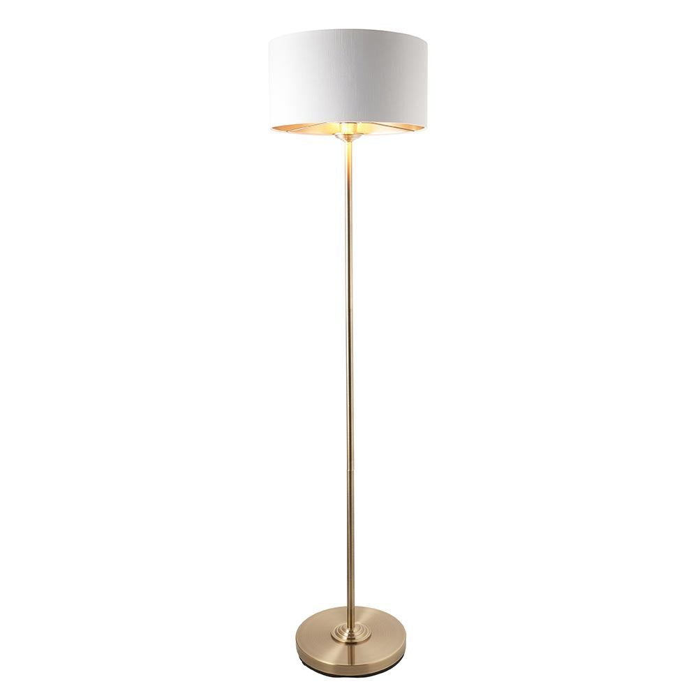 Endon Brenley floor lamp with brass stand, white drum shade and gold metallic inner, lit E27 fitting, on a plain white background.