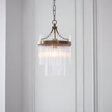 Endon Beaumont two-tier pendant in antique brass with clear glass rod fringe and chain suspension, hung against a white panelled wall.