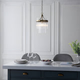 Endon Beaumont pendant in antique brass with tiered clear glass rods, hung from a chain above a kitchen island with grey chairs and panelled wall.