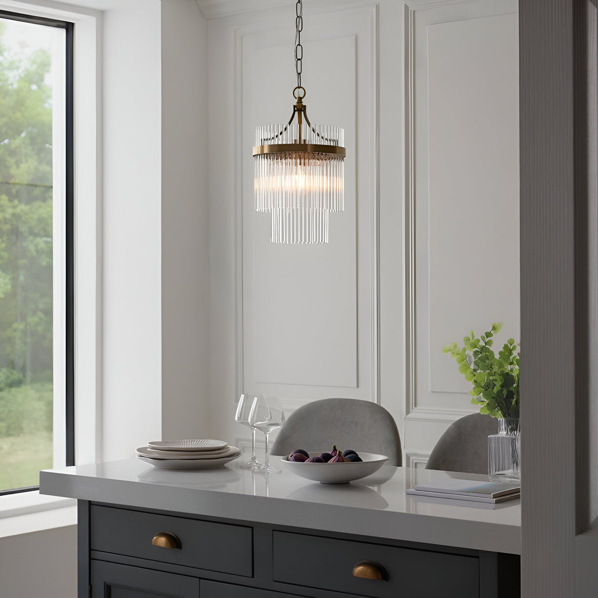 Endon Beaumont pendant in antique brass with tiered clear glass rods, hung above a grey kitchen island with dinnerware in a bright dining space.
