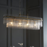 Beaumont 4 Light Linear Pendant in antique brass, an oval fixture lined with clear glass rods and four exposed bulbs, hung from chains in a dark panelled room.