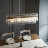 Beaumont 4 Light Linear Pendant in antique brass with clear glass rod fringe, hung above a dining table in a dark panelled room.