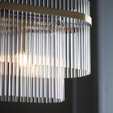 Close-up of the Beaumont 4 Light Linear Pendant in antique brass, showing clear glass rods hanging from the brass bar with a visible bulb glow.