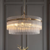 Endon Beaumont 7 Light Pendant in antique brass with tiered clear glass rods, hung from a chain against a panelled grey wall.